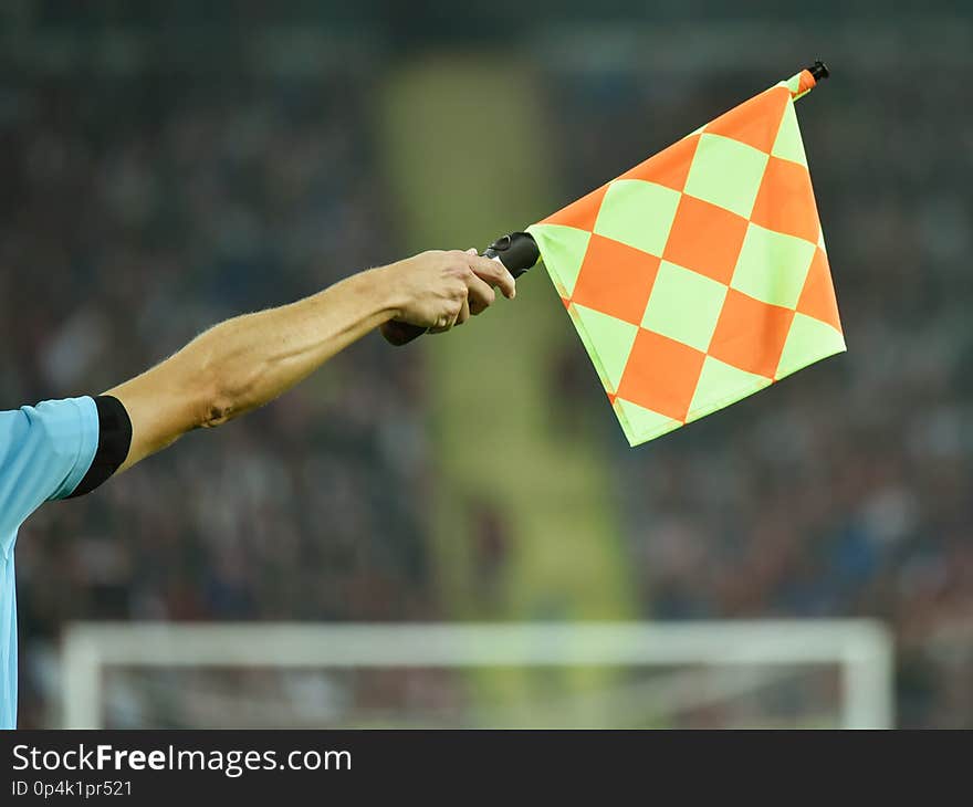 Raised hand with flag of assistant soccer referee with tribune in tha background