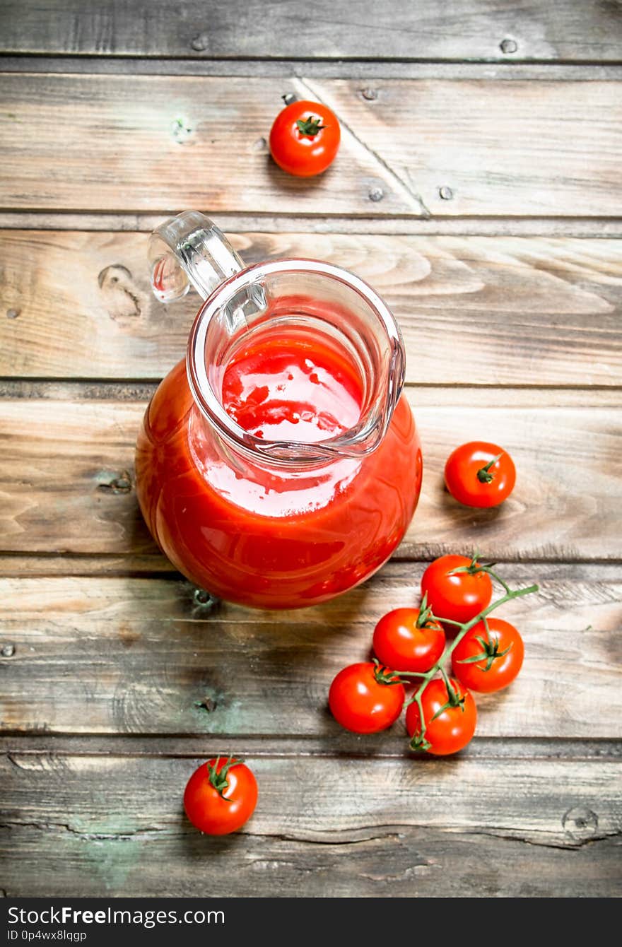 Tomato juice in a jug and fresh tomatoes. On wooden background