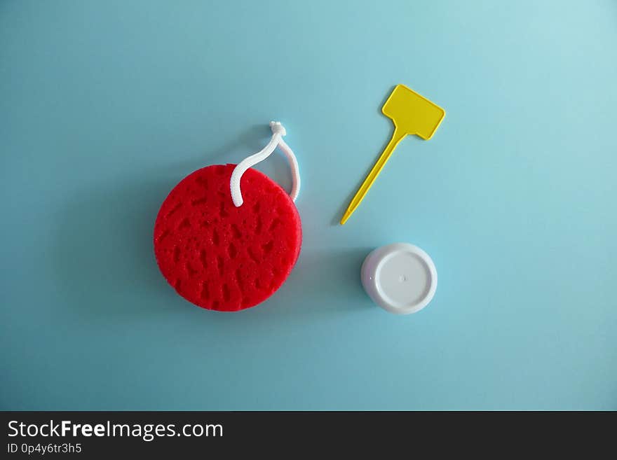 Red Bath Sponge, White Cream Box and Empty Yellow Label on a Light Blue Background