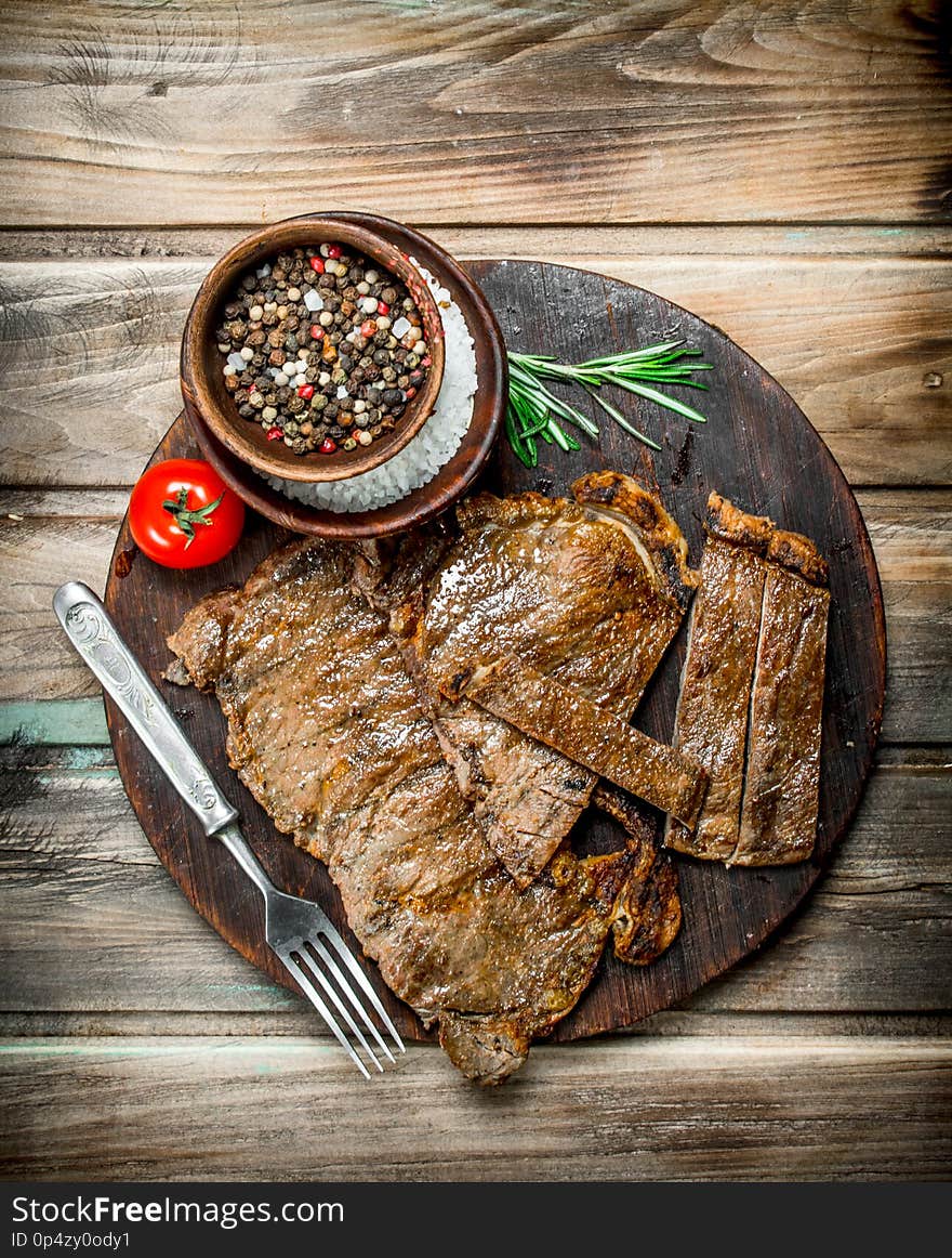 Grilled beef steaks with spices and rosemary. On a wooden background