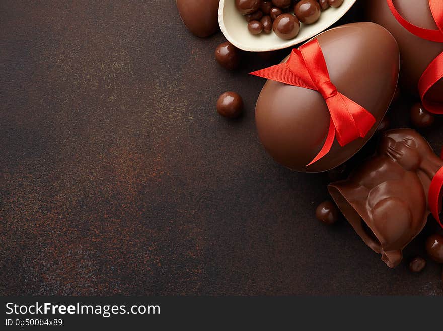 Easter composition with chocolate eggs and bunny decorated with red ribbon on dark brown background, holiday concept