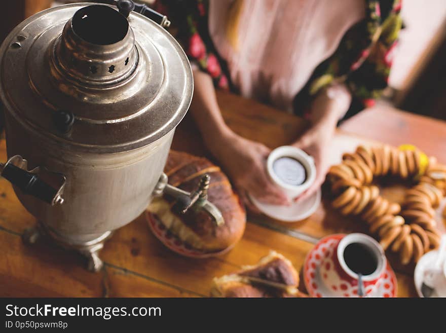 Tea, traditional Russian dishes and treats, a samovar on the table, the hands of a woman in a national kerchief are holding a cup