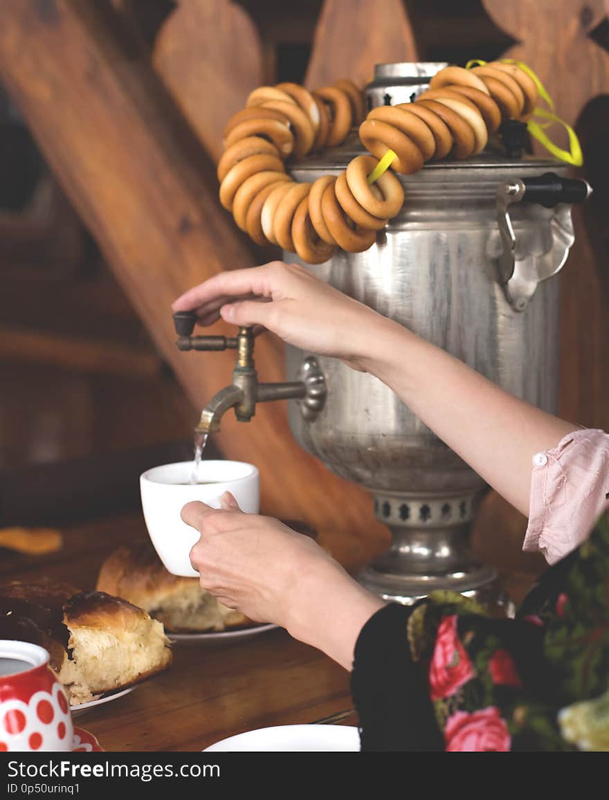 Women`s hands opened the tap of the samovar and took hot water in a mug of tea