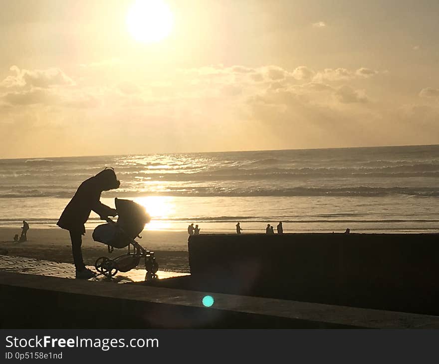 Mother love with small kid in baby carriage on the beach with romantic sunset.