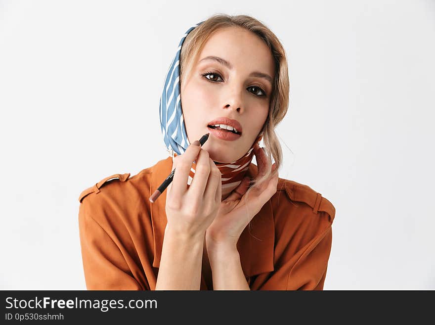 Image of a happy beautiful young woman wearing silk stylish scarf posing isolated over white wall background apply makeup with lip pencil