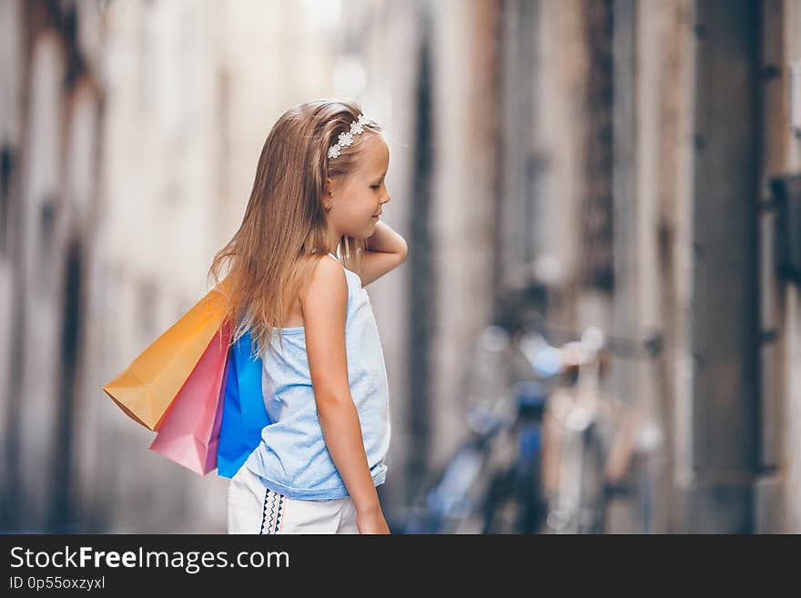 Portrait of adorable little girl walking with shopping bags outdoors in european city.