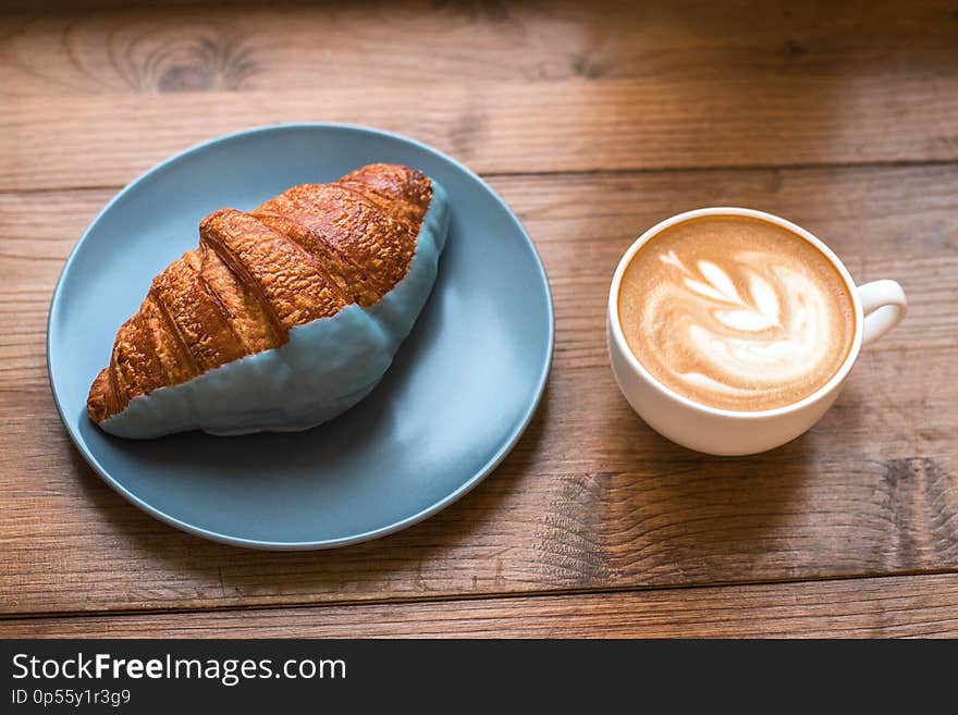 Cup of fresh cappuccino art and croissant on wooden background.