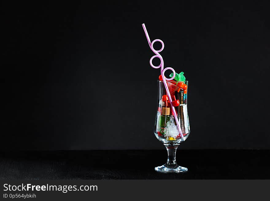 Coctail glass with plastic straw full of plastic and battery waste as imitation of real drink on horozontal black background with