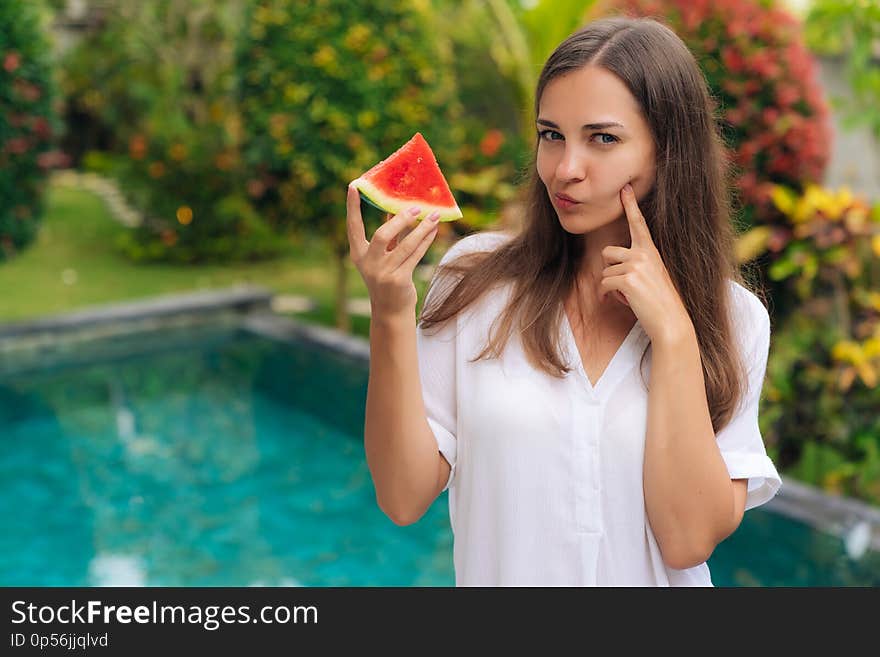 Portrait thoughtful girl with long hair holding slice of watermelon in her hand, thinking of eating or not eating fruit. Concept fresh, healthy food, vegetarian