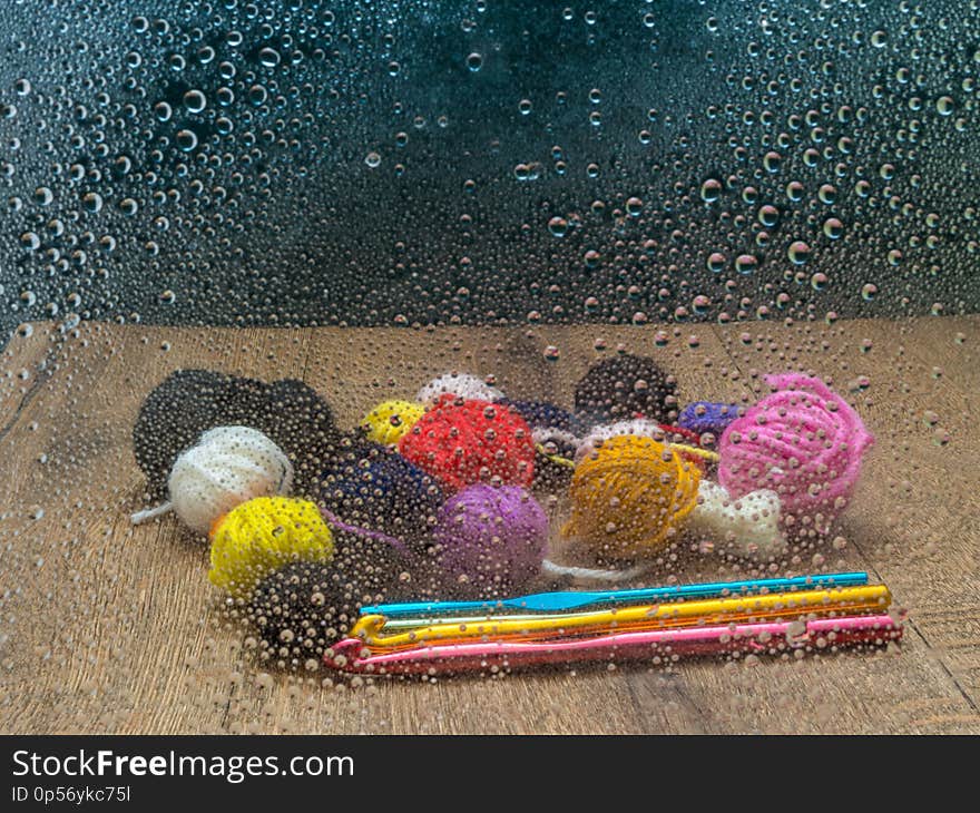 Looking in through the window. Small balls of left over wool on a wooden surface. The window has raindrops on it. Colorful crochet hooks. Looking in through the window. Small balls of left over wool on a wooden surface. The window has raindrops on it. Colorful crochet hooks.