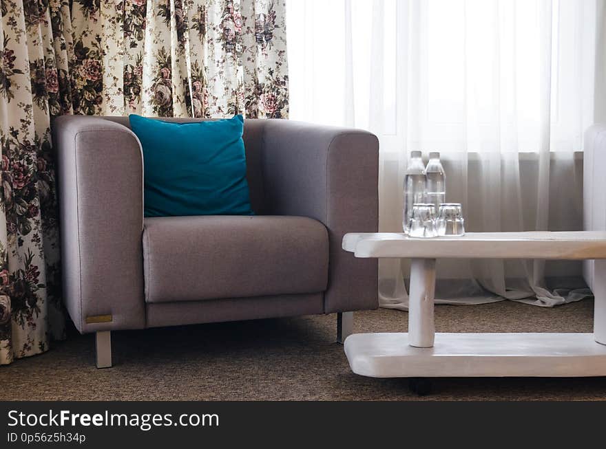 Interiors of the room in the hotel concept. A sofa with a blue pillow and a white table with water bottles.