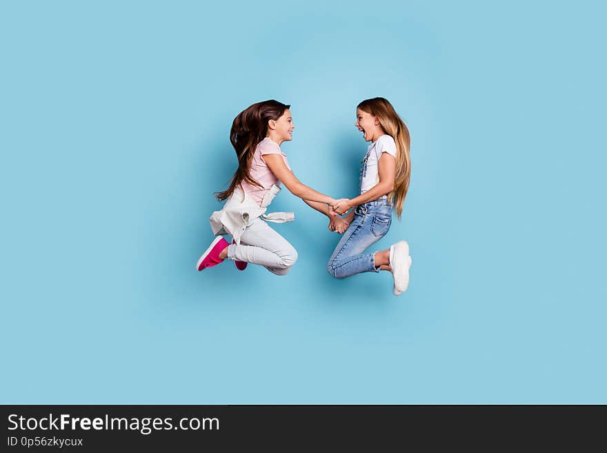 Full length body size profile side view of two people nice cute attractive cheerful straight-haired pre-teen girls having fun great weekend holding hands isolated over blue pastel background.