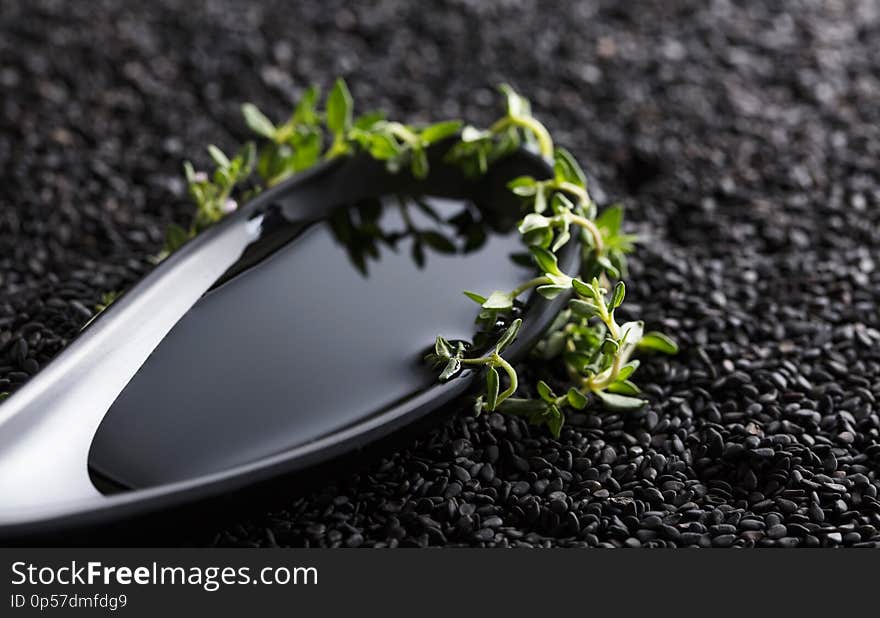 Vegetable oil in small bowl with thyme branches on a background of black sesame. Selective focus