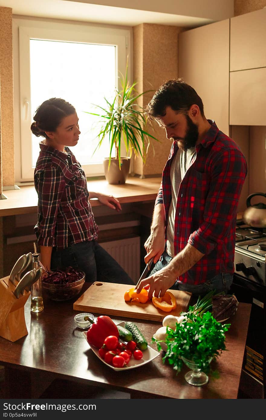 Beautiful young couple in kitchen at home while cooking healthy food. Man cuts a pepper. Woman looks at her husband. Scene from family life. Vertically framed shot