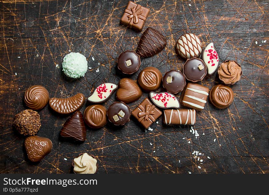 Chocolate sweets with nuts and various fillings. On a wooden background