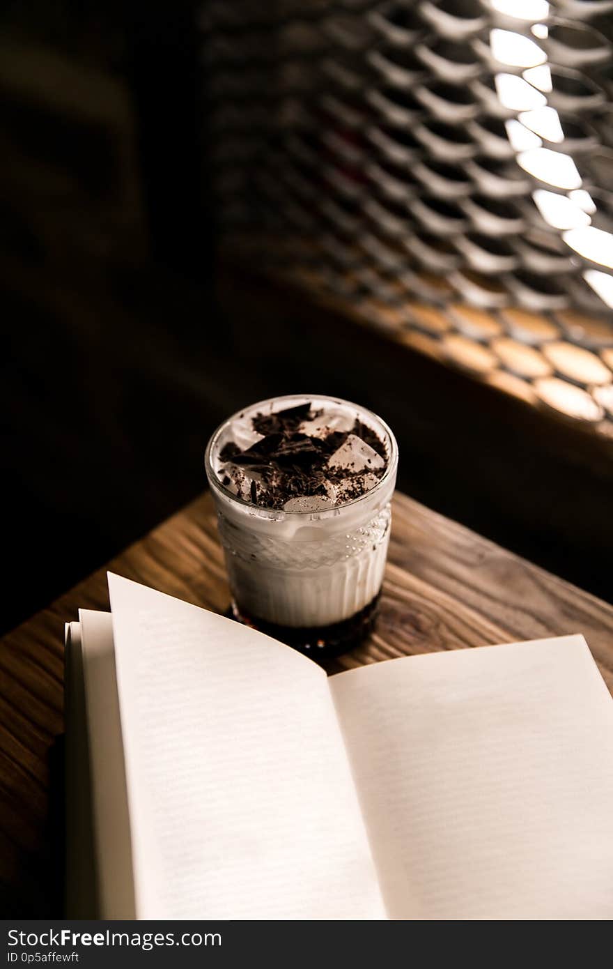 Close-up on a brown wooden table with coffee and cream, next to it is a book. Close-up on a brown wooden table with coffee and cream, next to it is a book.