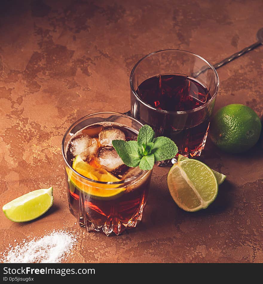 Cocktail of rum and cola ice cubes and lime in glass goblets on a dark brown background. Strong alcoholic drink.