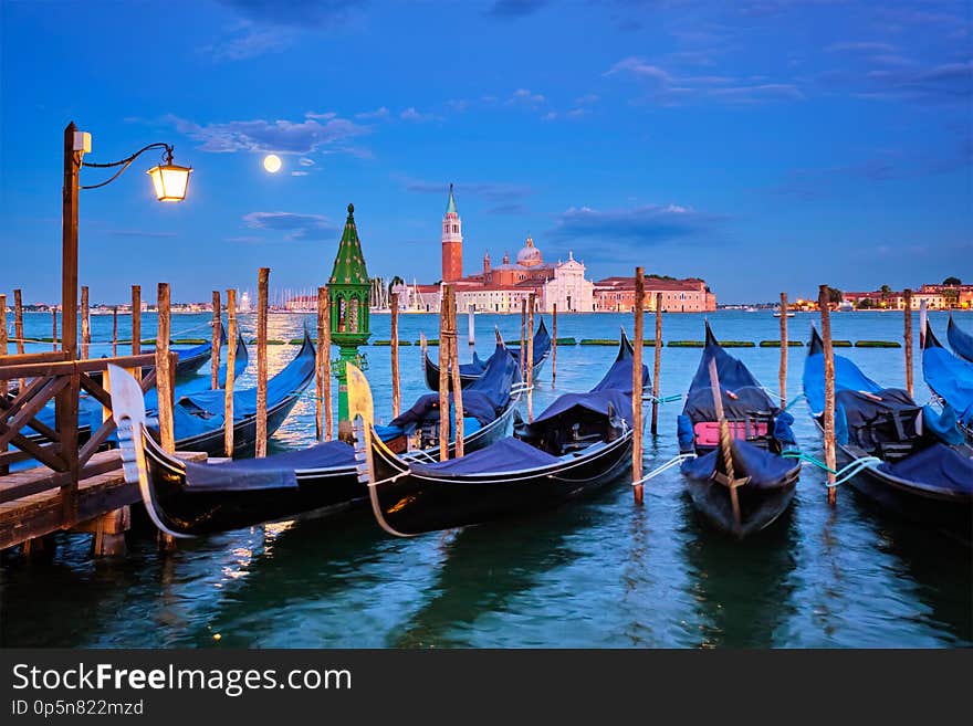 Romantic vacation Venice travel background - gondolas at Saint Mark San Marco square and Basilica San Giorgio Maggiore Church seen across Venice lagoon with full moon. Venice, Italy. Romantic vacation Venice travel background - gondolas at Saint Mark San Marco square and Basilica San Giorgio Maggiore Church seen across Venice lagoon with full moon. Venice, Italy