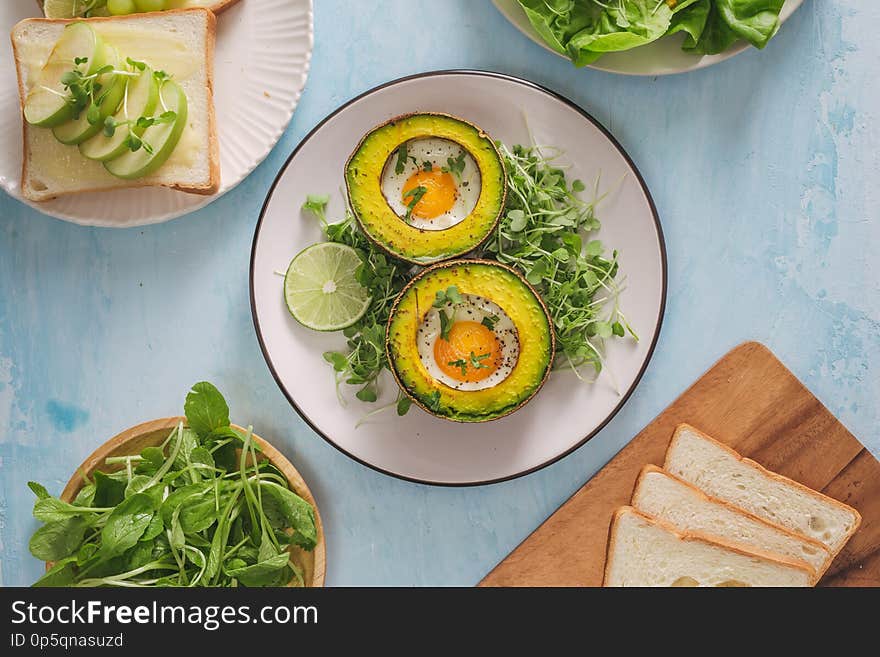 Healthy vegan breakfast. Diet. Baked avocado with egg and fresh salad from arugula, toast and butter. On a white marble plate, a