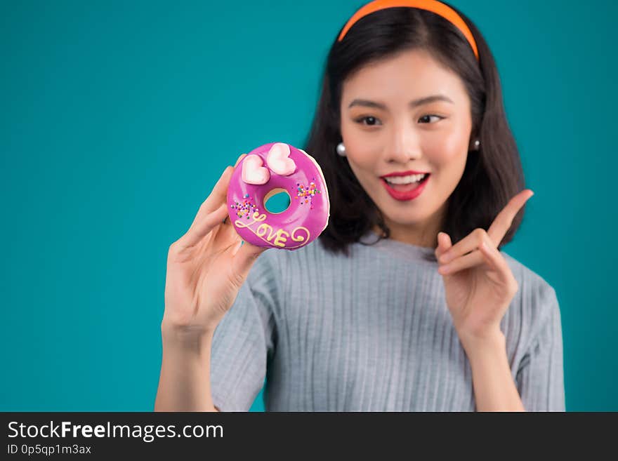 Asian beauty girl holding pink donut. Retro joyful woman with sweets, dessert standing over blue background.