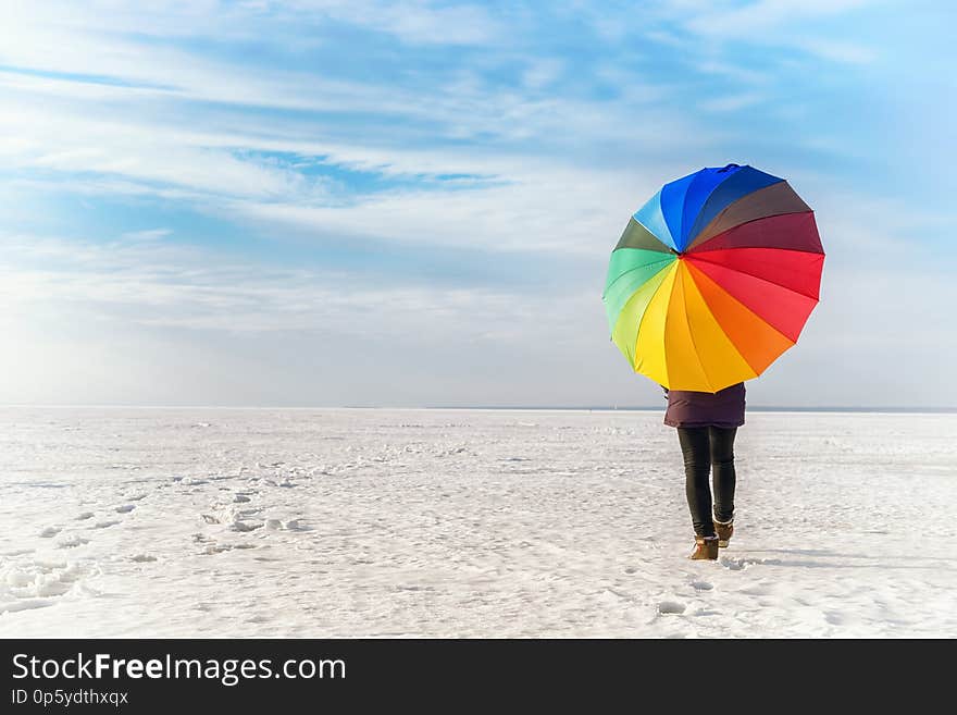 Woman with rainbow colored umbrella walking on frozen sea. Bright colored winter landscape