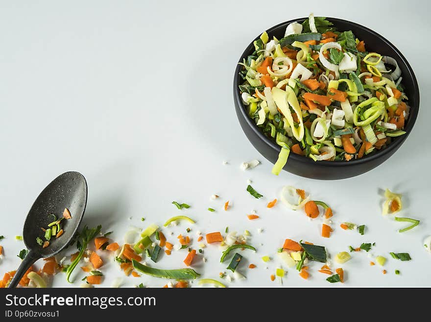 Black bowl with soup or wok ingredients, vintage spoon and messy vegetables. White background, space for text. Black bowl with soup or wok ingredients, vintage spoon and messy vegetables. White background, space for text