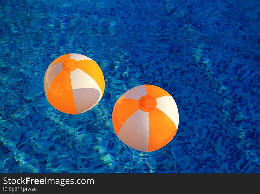 Two rubber air yellow white inflatable balls and toy for swimming pool in transparent blue water. Beach balls floating on water.