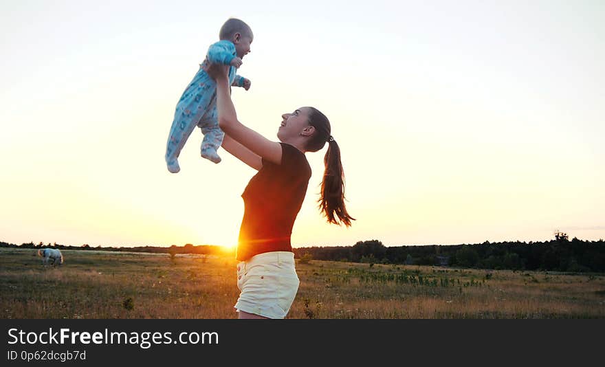 Emotional young woman raising her baby in hands in a field at sunset in slo-mo