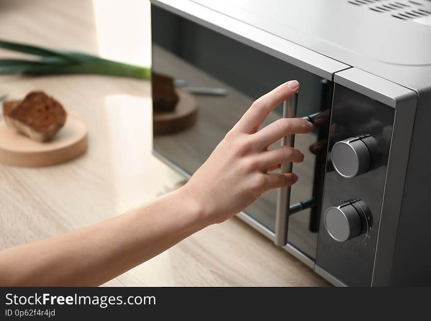 Young woman using microwave oven on table