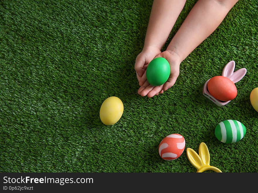 Little child holding painted Easter egg on green grass, top view. Space for text