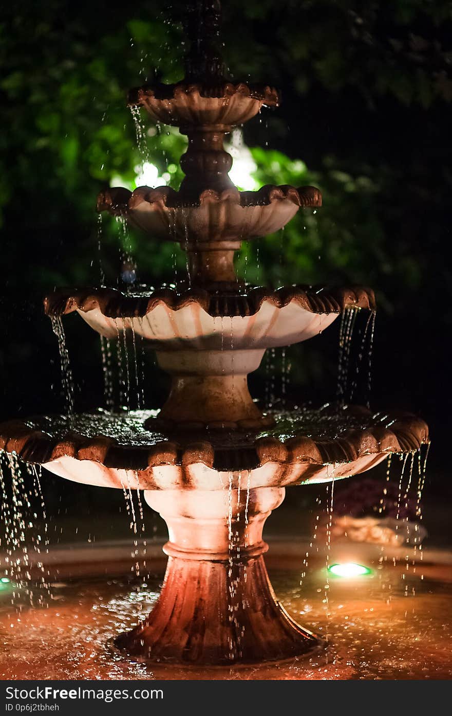 The fountain in a garden in the evening by the light of lamps. Romantic atmosphere. Water flows and splashes in the fountain. The fountain in a garden in the evening by the light of lamps. Romantic atmosphere. Water flows and splashes in the fountain