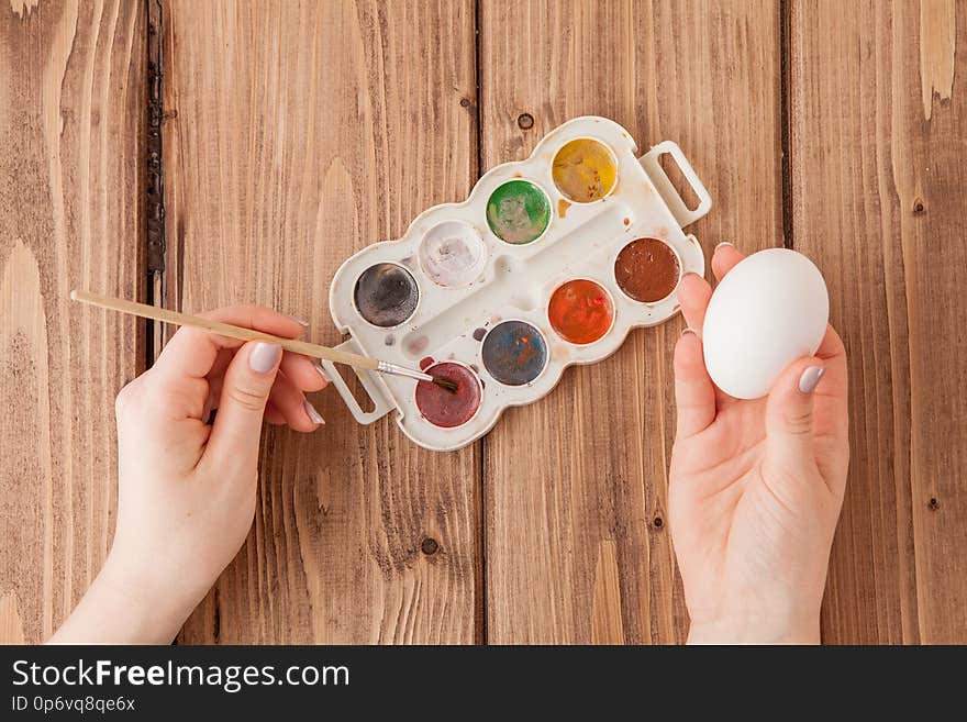 Close-up Of Woman`s Hands Painting An Easter Egg On Wooden Background