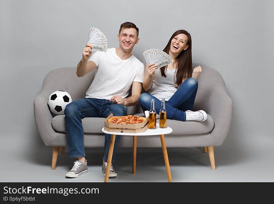 Cheerful couple woman man football fans cheer up support favorite team holding fan of money in dollar banknotes, cash