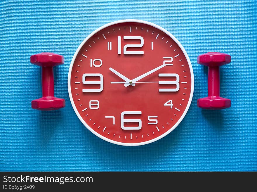 Time for exercising clock and dumbbell with yoga mat background, top view