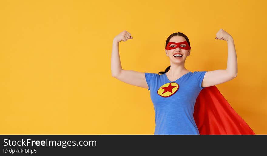 Joyful beautiful young woman in superhero costume posing on yellow background