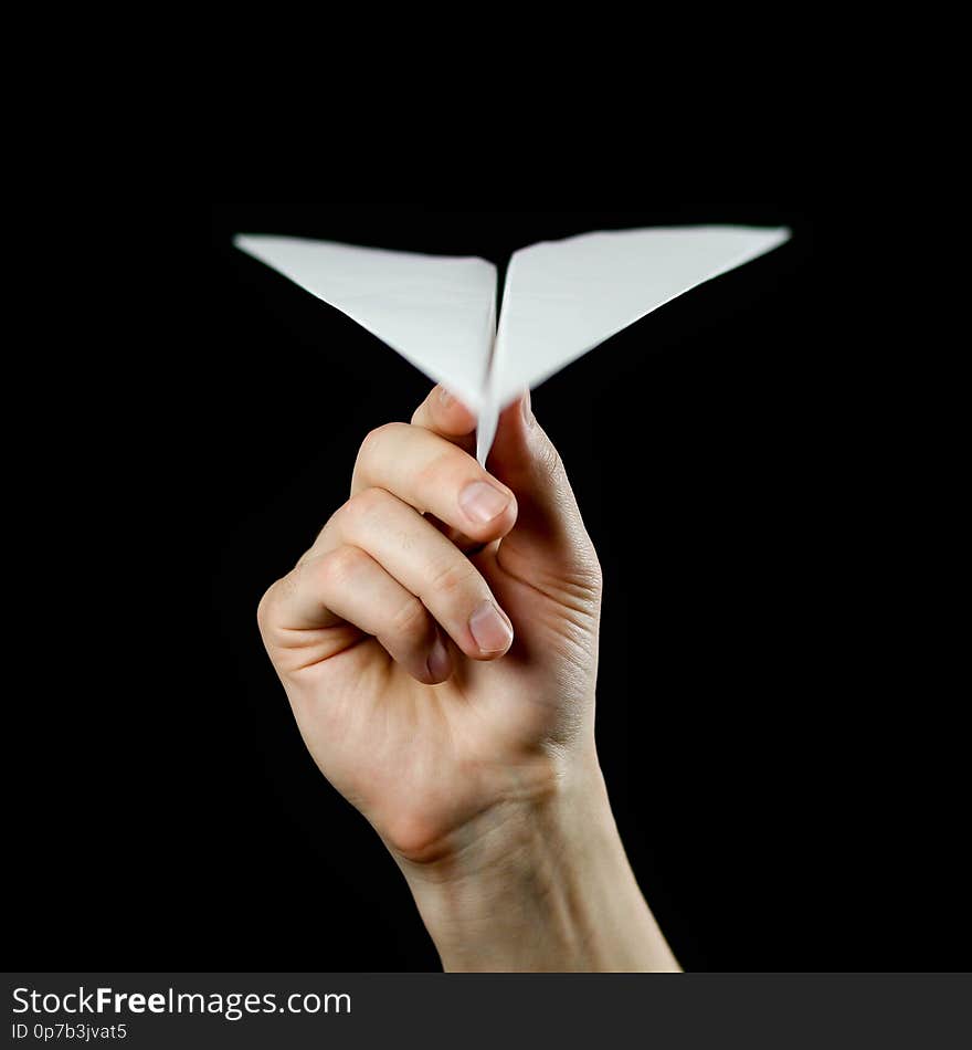 Hand holding a white paper airplane. Close up. Isolated on black background.