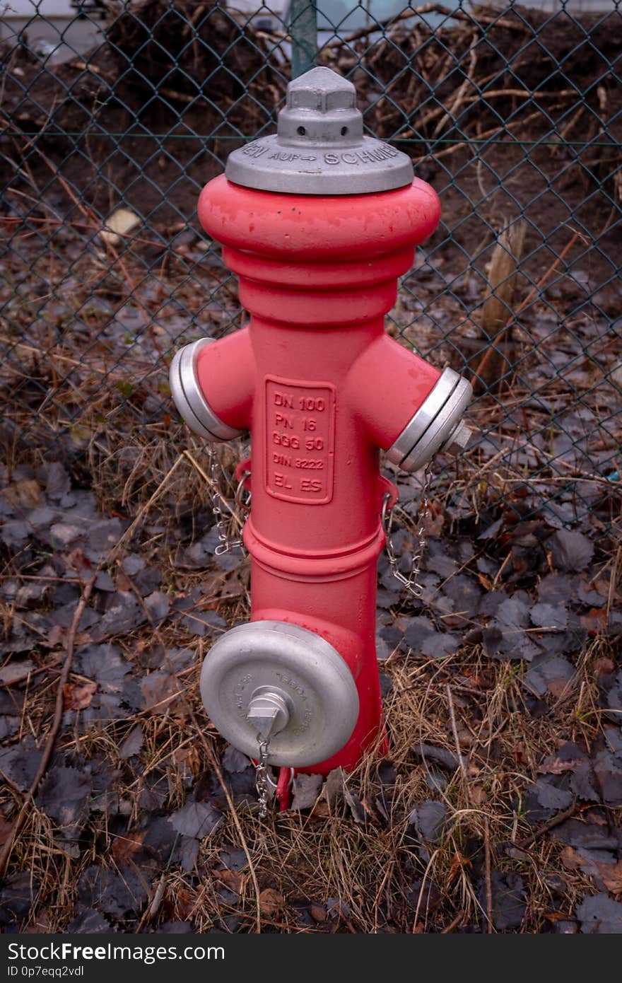 A red hydrant stands in front of a fence