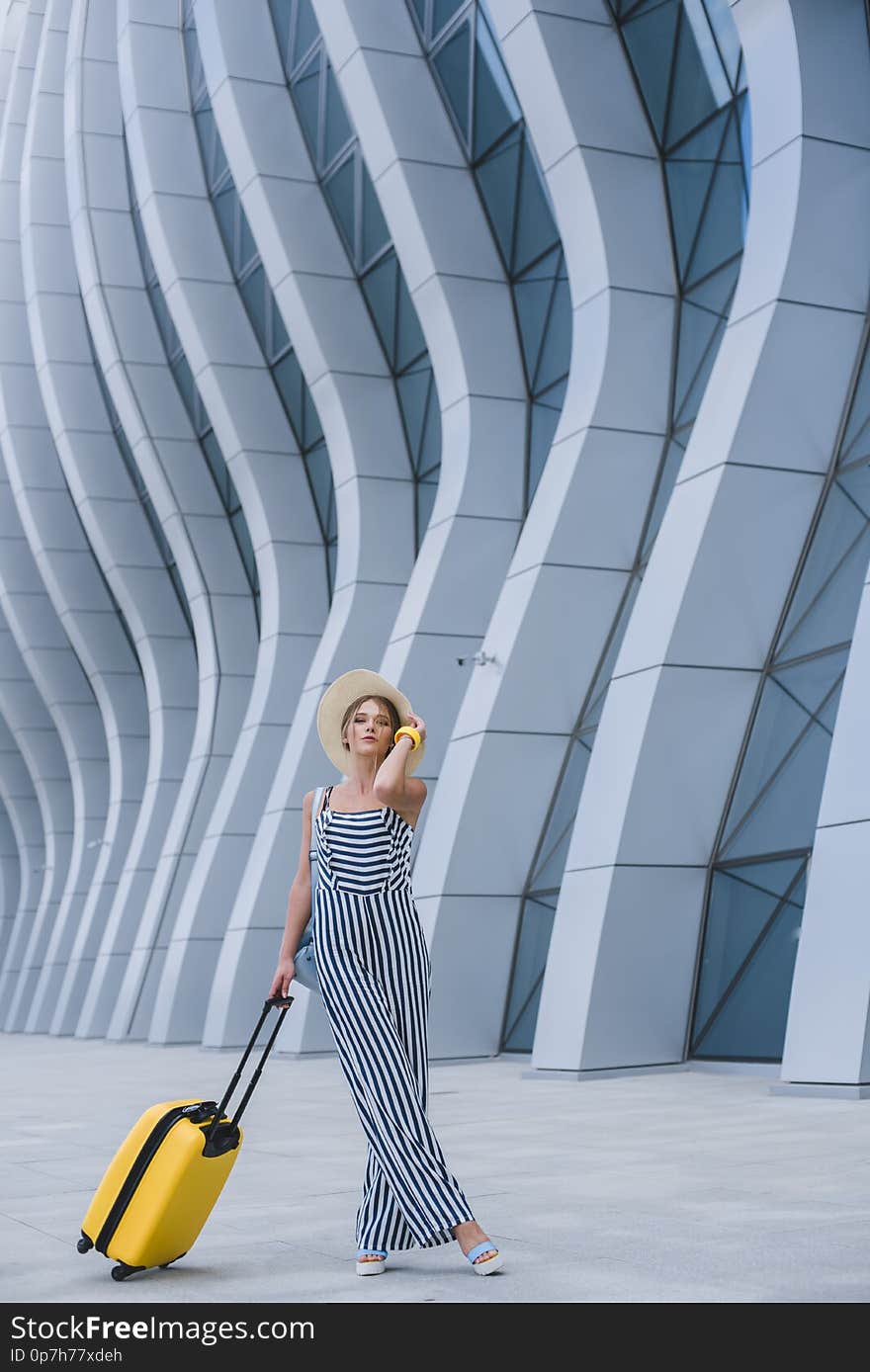 Beautiful young stylish Caucasian woman at the airport with a yellow suitcase and a straw hat goes on a journey. Beautiful young stylish Caucasian woman at the airport with a yellow suitcase and a straw hat goes on a journey.