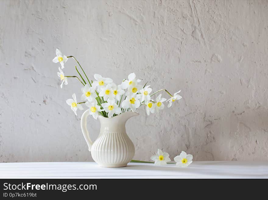 White daffodils in jug on white background