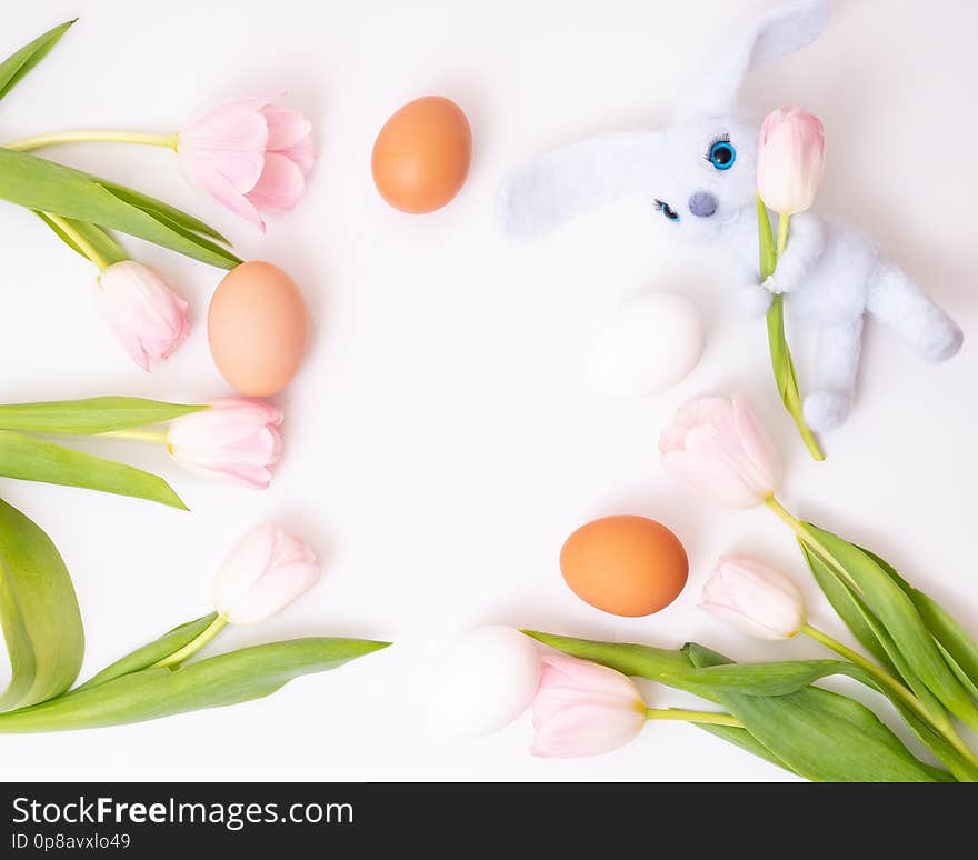 Blue toy rabbit three colored eggs mixed with pink tulips. Top view