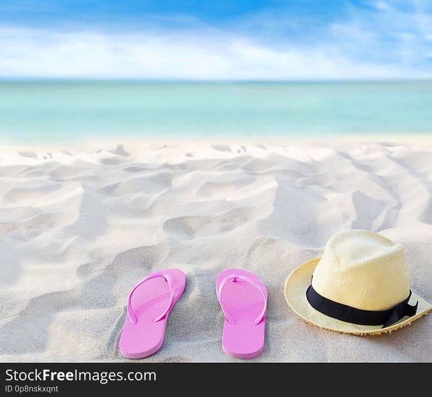 Beach summer holiday background. Flip flops and hat on sand near ocean. Summertime accessories on seaside. Tropical vacation and relax travel concept. Top view and copy space. Selective focus