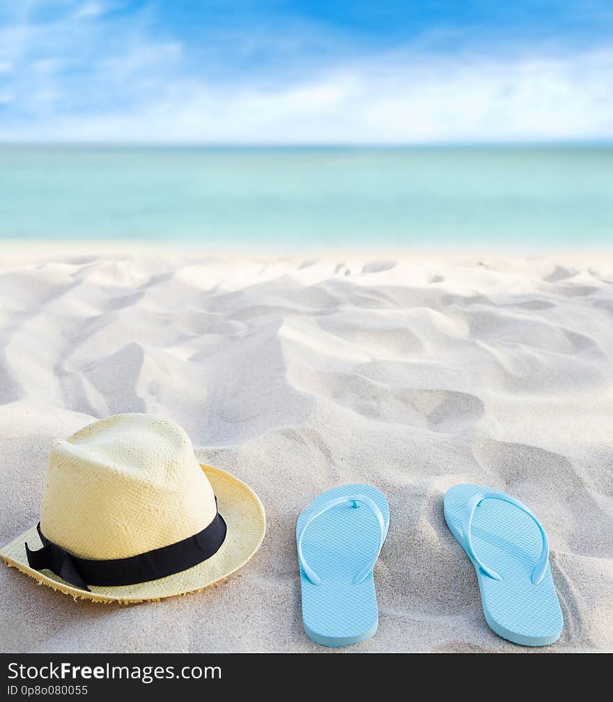 Beach summer holiday background. Flip flops and hat on sand near ocean. Summertime accessories on seaside. Tropical vacation