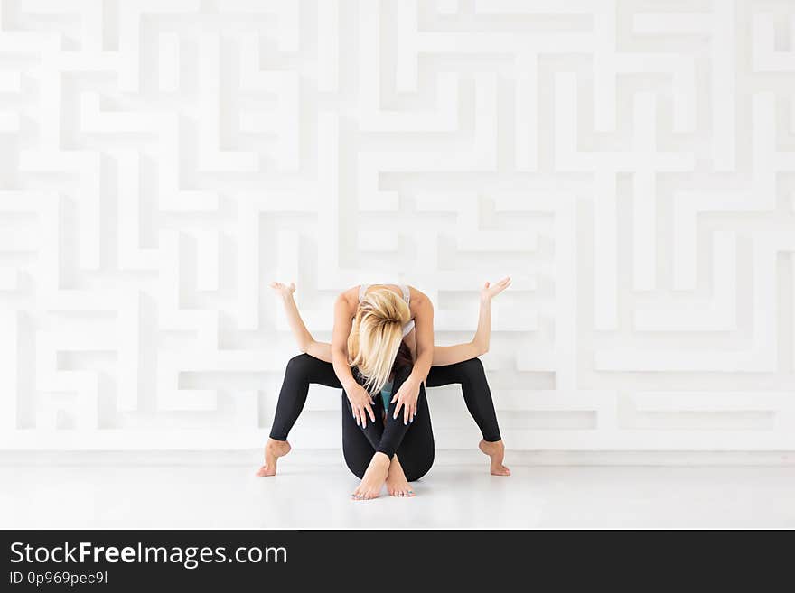 Two young women practicing acro yoga in white studio