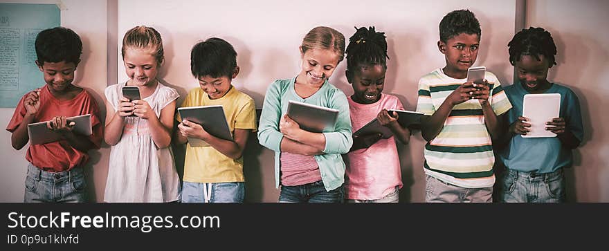 Happy pupils standing with technology against wall in classroom