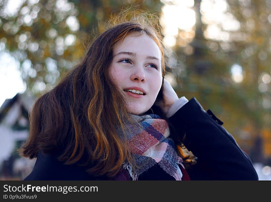 A beautiful girl with reddish hair smiles and removes a long strand of hair over her shoulder, being in the Park in the cold season