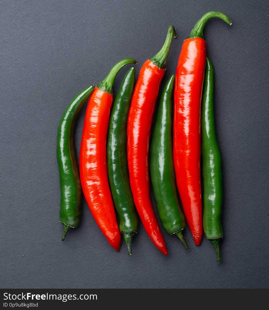 Green and red chili peppers on black background top view. Hot spicy food.