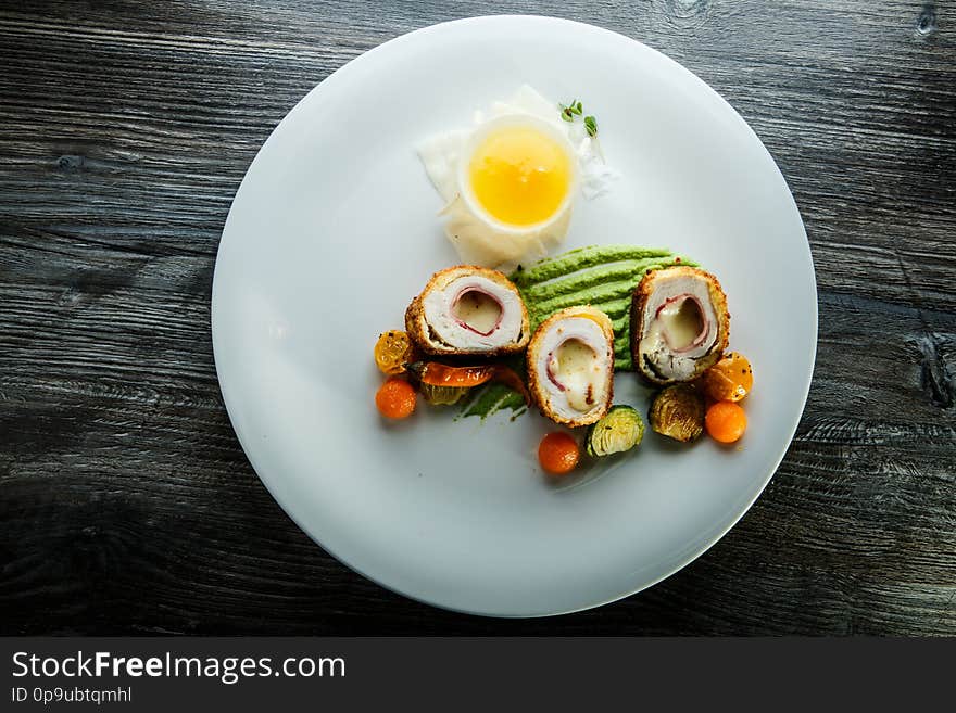 Top view dissected chicken Kiev cutlets served with grilled peppers, tomatoes cherry, brussels sprouts, spinach puree and sauce on white plate. Top view dissected chicken Kiev cutlets served with grilled peppers, tomatoes cherry, brussels sprouts, spinach puree and sauce on white plate