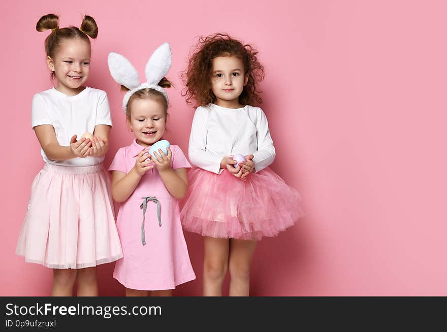 Three smiling dressed up for the holiday kid girls hold painted eggs on Easter day