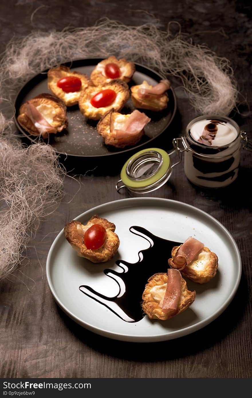 Few puff pastry cups filled by cheese and ham on blue plate with dark sauce