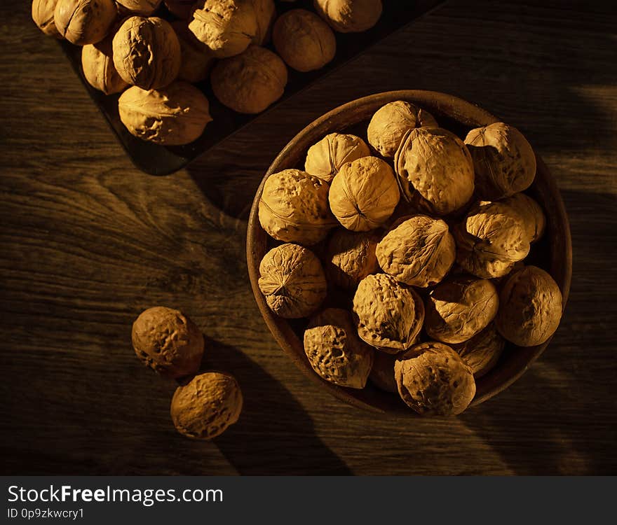 Walnuts lie in a bowl, next to them are scattered nuts on a wooden table. Walnuts lie in a bowl, next to them are scattered nuts on a wooden table